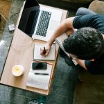 man in black t-shirt sitting at the table using macbook pro